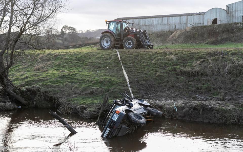 A tractor is holding the 4x4 by a strap so the vehicle doesn't move any further down the river.
