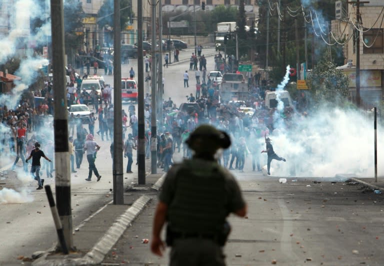 A member of Israeli security forces stands guard in front of Palestinian protesters throwing stones during clashes on October 13, 2015 in the West Bank city of Bethlehem