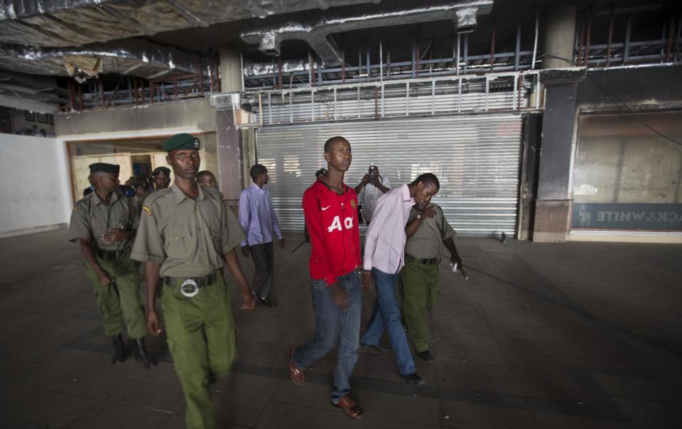 Ethnic Somalis Liban Abdullah Omar, center-left, and Mohamed Ahmed Abdi, center-right, who are accused of aiding the Westgate Mall gunmen, are escorted by police around the mall in Nairobi, Kenya Tuesday, Jan. 21, 2014. Court officials and four handcuffed ethnic Somalis accused of aiding the gunmen who attacked Nairobi's Westgate Mall in Sept. 2013, walked through the heavily damaged shopping center on Tuesday led by Chief Magistrate Daniel Ochenja, to help the court visualize the mall's layout for the ongoing trial of the four men. (AP Photo/Ben Curtis)