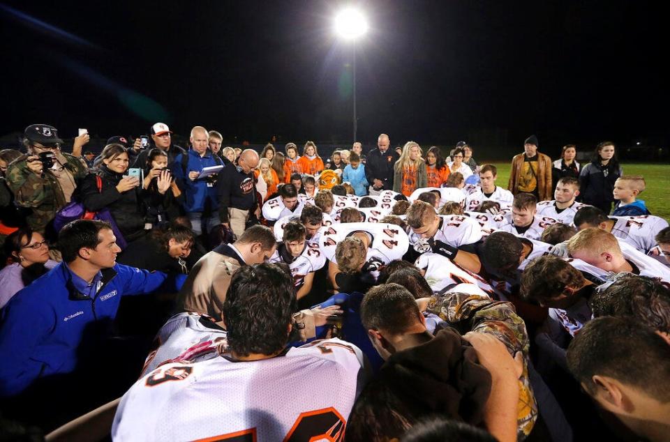 Bremerton assistant football coach Joe Kennedy, obscured at center in blue, is surrounded by Centralia High School football players as they kneel and pray with him on the field after their game against Bremerton on Oct. 16, 2015, in Bremerton, Wash.