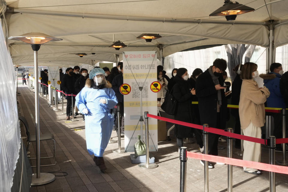 A medical worker runs to guide people as they wait for their coronavirus test at a makeshift testing site in Seoul, South Korea, Friday, Jan. 28, 2022. (AP Photo/Ahn Young-joon).