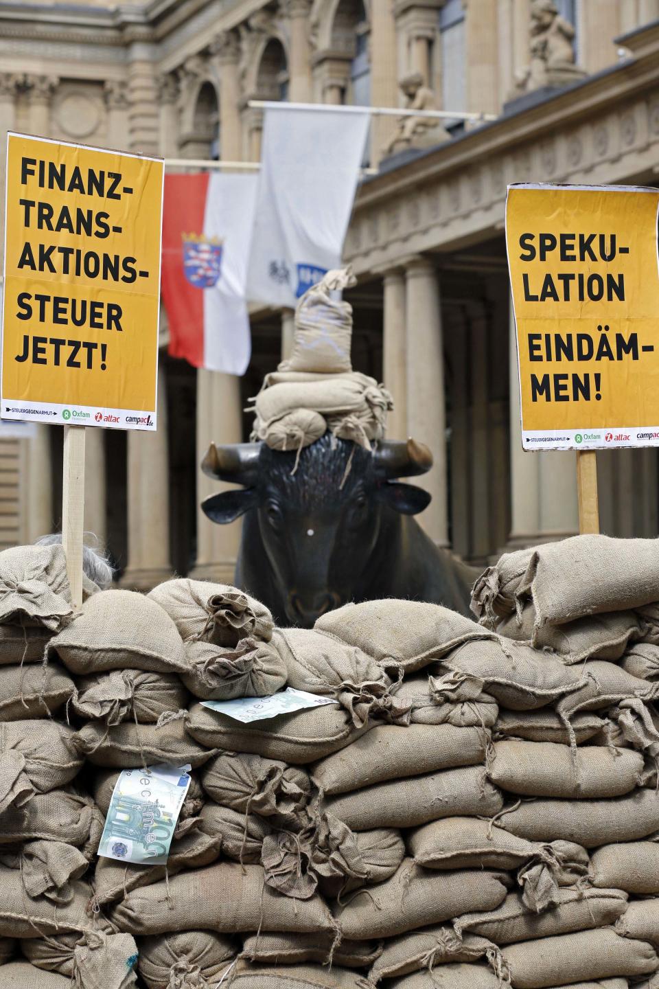 The sculpture of the bull is surrounded sandbags outside the Frankfurt stock exchange to demonstrate against the government financial policy in Frankfurt, central Germany, Sunday June 17, 2012. About 200 activists with the anti-globalization group Attac participated in the protest calling for a tax on financial transactions have erected a wall of sandbags outside the Frankfurt stock exchange. White spot at the bull's nose is a sticker. Poster at right reads: Stem Speculations, and at left: Transaction Tax Now. (AP Photo/dapd/Mario Vedder)