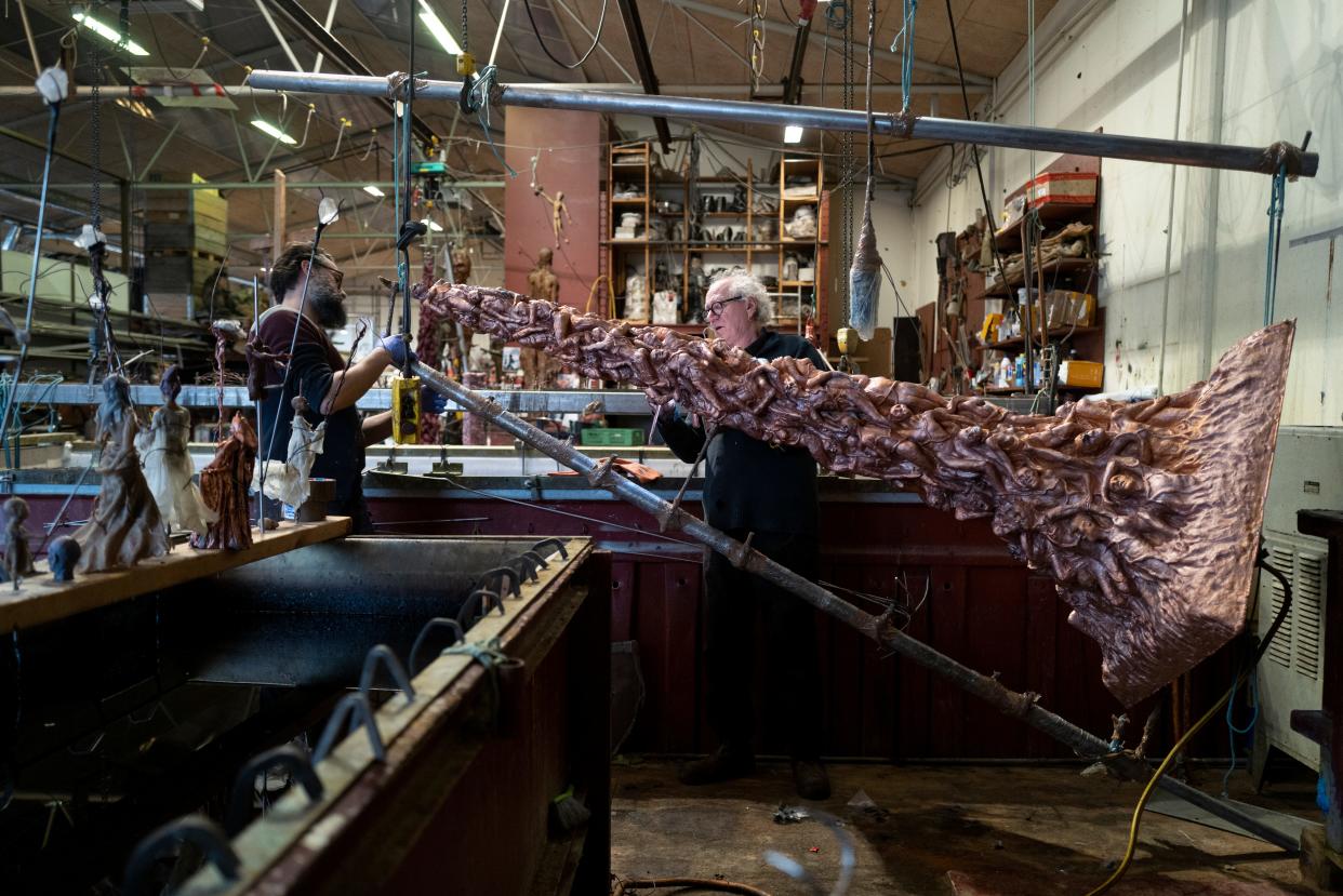 Two men use tools to prop up the Pillar of Shame sculpture.