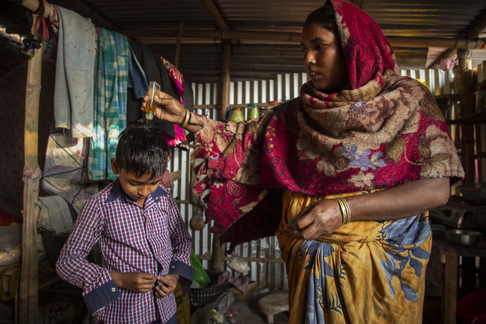 Imradul Ali, 10, left, wears a shirt as his mother Anuwara Beghum, 30, pours oil on his head as he prepares to leave for school from his rented kitchen cum bedroom on the outskirts of Gauhati, India, Friday, Feb. 5, 2021. Once school is done for the day, Ali, rushes home to change out of his uniform so that he can start his job as a scavenger in India’s remote northeast. Coming from a family of scavengers or “rag pickers," Ali started doing it over a year ago to help his family make more money. Ali says he doesn’t want to spend his life doing this, but he doesn’t know what the future holds. (AP Photo/Anupam Nath)