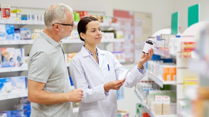 medicine, pharmaceutics, health care and people concept - happy pharmacist and senior man customer with drug and prescription at drugstore.