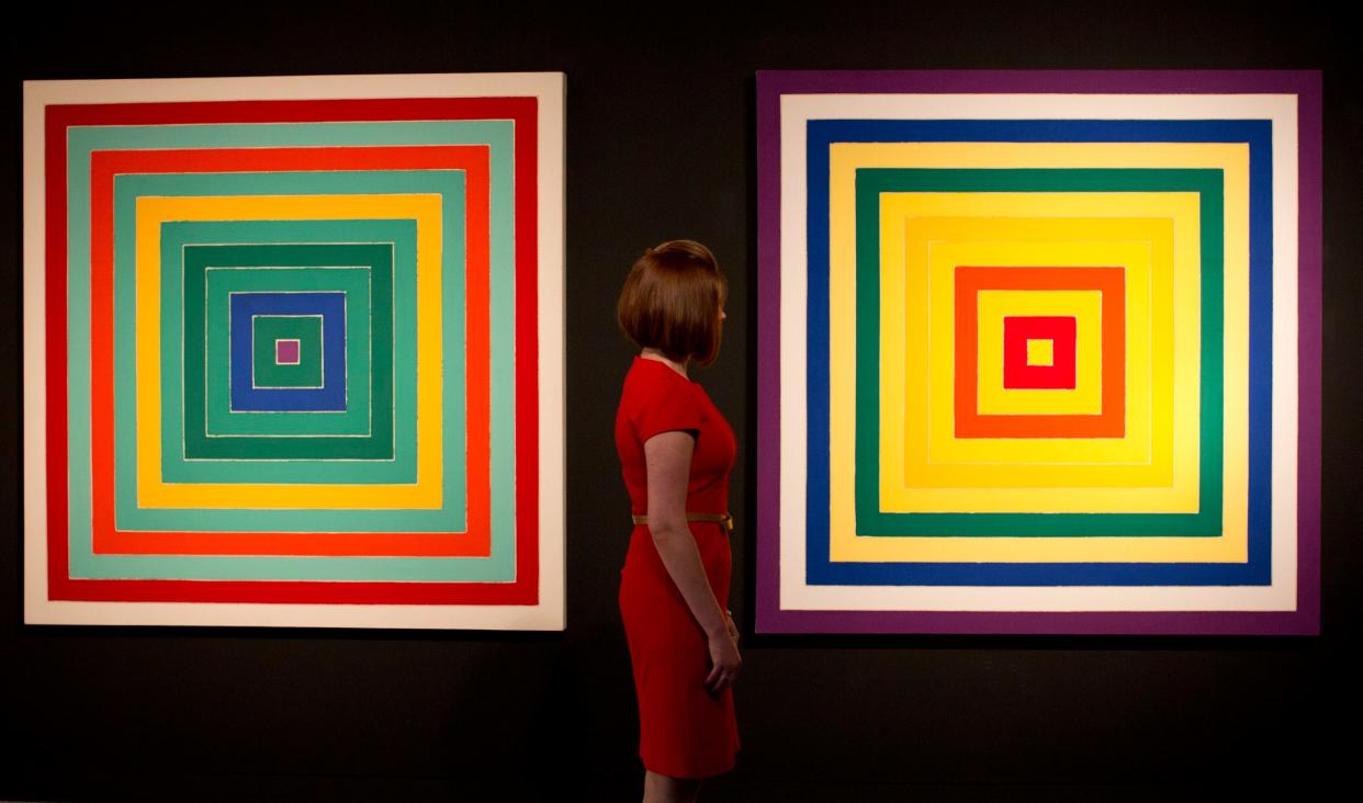 A gallery employee with two works by Stella from the 1970s, 'D. Scramble: Ascending Green Values/Ascending Spectrum', left, and 'I. Scramble: Ascending Yellow Values/Descending Spectrum'