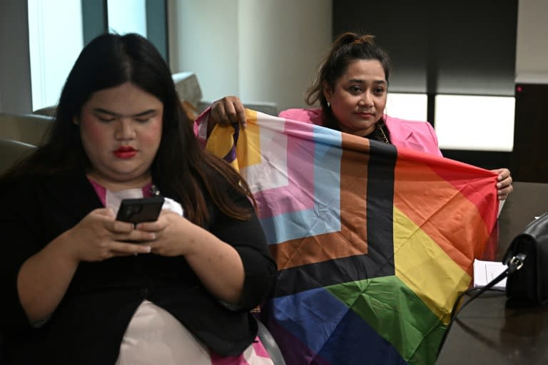 La activista LGBTQ Ann Waddao Chumaporn (drcha.) muestra una bandera de orgullo gay junto a la también activista Chanya Rattanatada en la sede del Parlamento tailandés, en Bangkok, el 2 de abril de 2024 (Lillian Suwanrumpha)