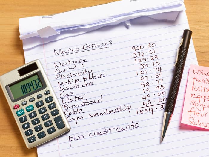 A notepad showing monthly expenses including mortgage, car, electricity, mobile phone, insurance, groceries, gas, water, broadband, cable, gym membership, and credit cards. A calculator and pen are also shown