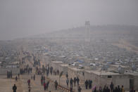 Syrians walk along in a refugee camp for displaced people run by the Turkish Red Crescent in Sarmada district, north of Idlib city, Syria, Friday, Nov. 26, 2021. Row upon row of tents, brick homes and other structures with water tanks on top dot the town of Sarmada near the border with Turkey, making up a series of huge informal refugee camps. Women cook, children play, men go to work, pray and discuss politics. Most of the inhabitants are displaced from various bouts of violence in Syria's 10-year conflict. (AP Photo/Francisco Seco)