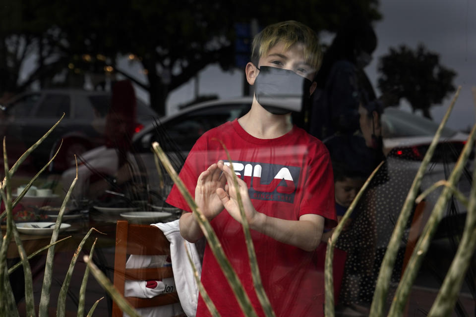 FILE - In this May 13, 2021, file photo, a child wears a mask while looking out the window of a beachfront restaurant in Santa Monica, Calif. A number of states immediately embraced new guidelines from the CDC that say fully vaccinated people no longer need to wear masks indoors or out in most situations. But other states - and some businesses _ are taking a wait-and-see attitude. (AP Photo/Marcio Jose Sanchez, File)