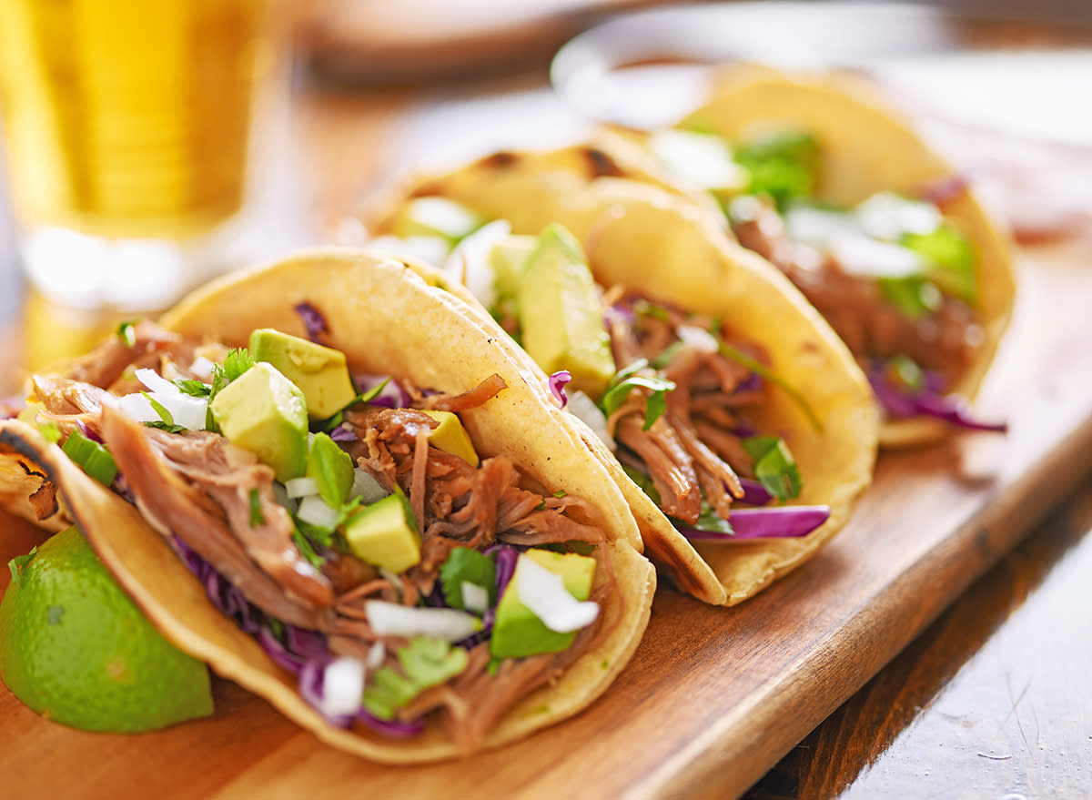 three pork carnitas street tacos in yellow corn tortilla with avocado, onion, cilantro and cabbage