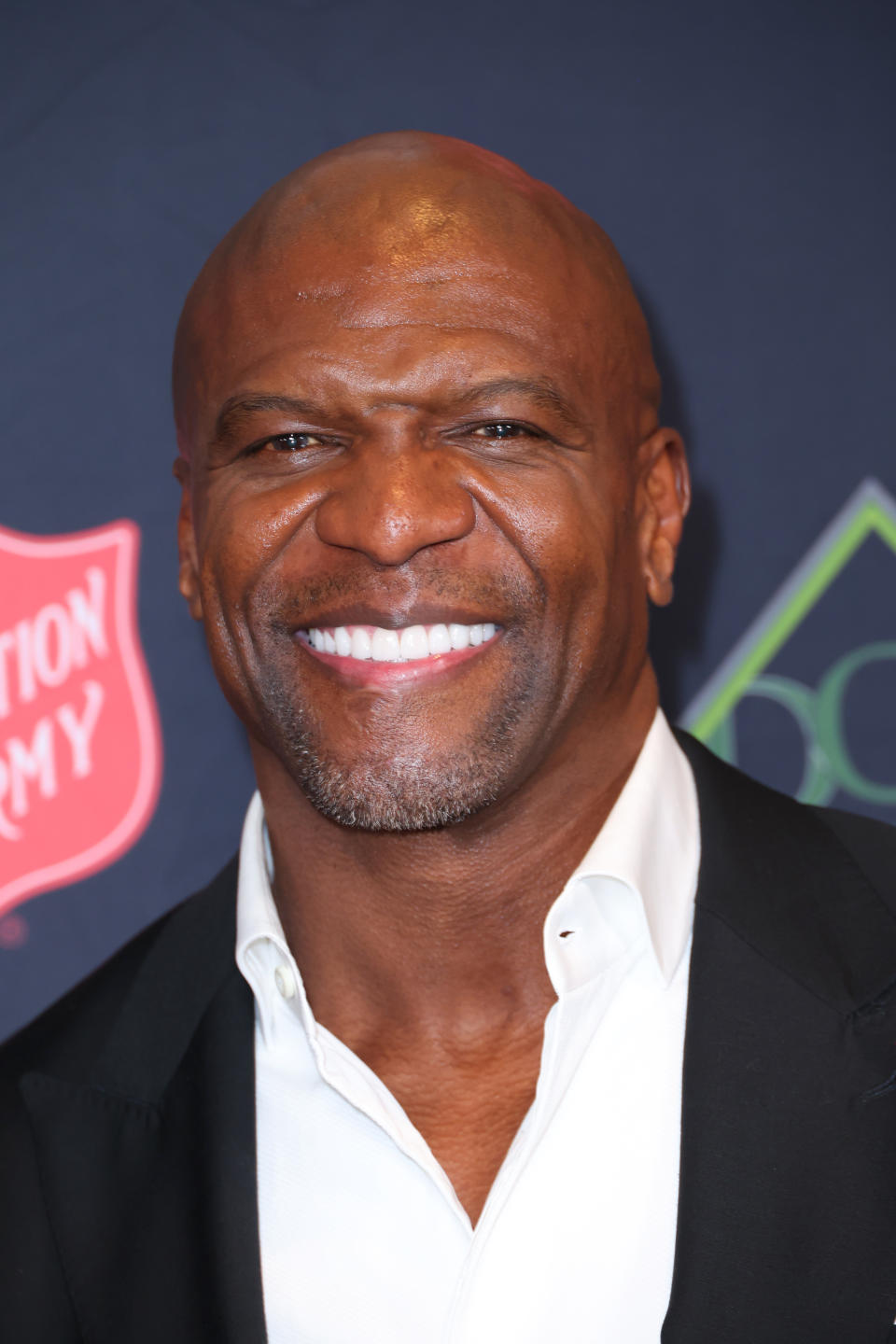 Terry Crews smiles at a red carpet event, wearing a white dress shirt and black blazer. 