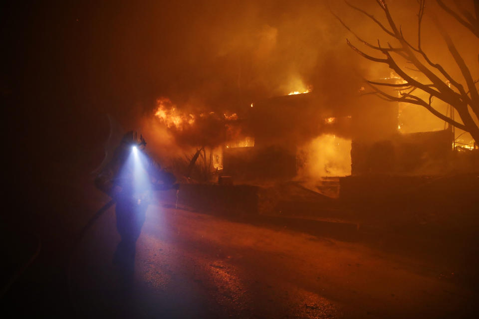 A firefighters gets in position to hose down flames as a home burns in the Getty fire area along Tigertail Road, Oct. 28, 2019, in Los Angeles. (AP Photo/Marcio Jose Sanchez)