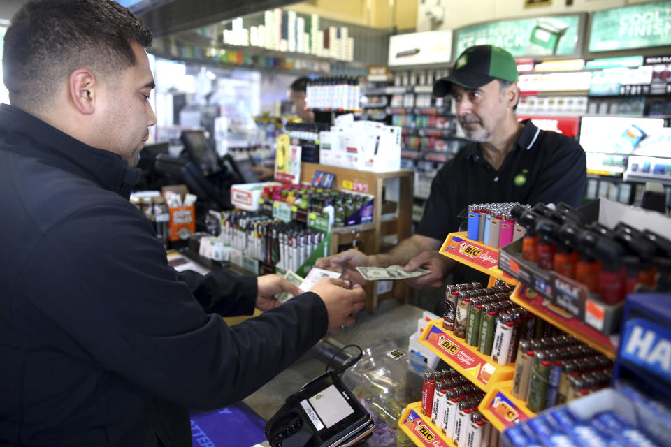 Clerk Zoheir Jendo, right, sells lottery tickets to Jose Reyna of Hampshire at the Stark's Corner Market BP gas station in Pingree Grove, Ill. Monday, Oct. 22, 2018. (Patrick Kunzer/Daily Herald via AP)