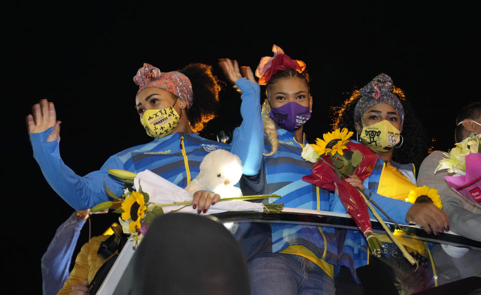 Olympian athletes Neisi Dajomes, left, who won the gold in women's weightlifting 76kg at the 2020 Tokyo Olympics, teammates Angie Palacios, center, and 87kg silver medalist Tamara Salazar, wave from the top of a bus as they arrive at Atahualpa Stadium in Quito, Ecuador, Wed, Aug. 4, 2021. (AP Photo/Dolores Ochoa)