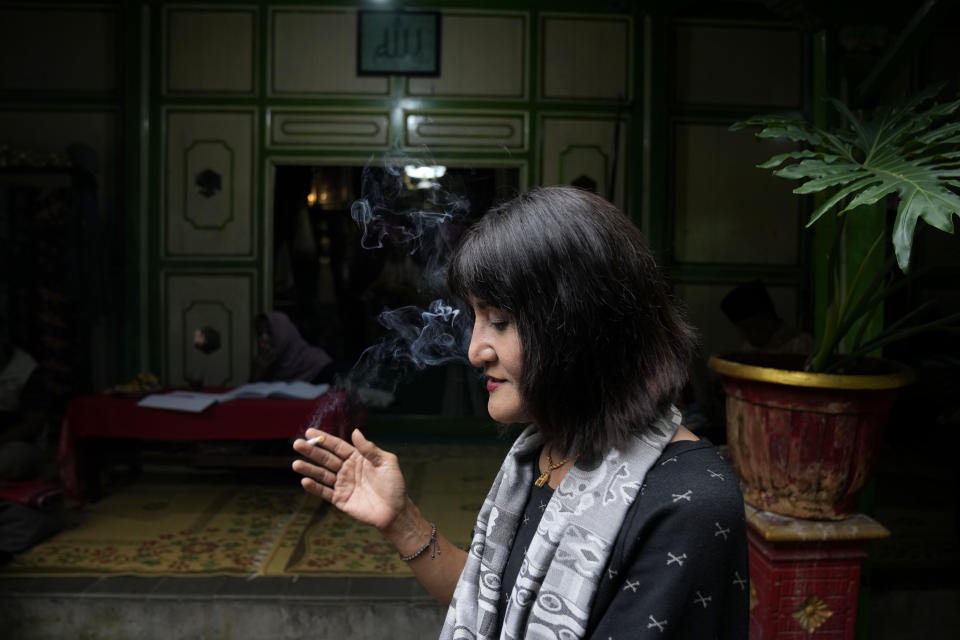 Y.S. Al Buchory, a trans woman, smokes a cigarette during an interview, with Arabic calligraphy that reads "Allah" above an entrance at Al Fatah Islamic school in Yogyakarta, Indonesia, Sunday, Nov. 6, 2022. Buchory, 55, struggled for years to cope with lack of acceptance by people around her, but now feels at home at the school. “Like a rainbow, if there are red, yellow, green colors combined, it becomes more beautiful, rather than only black and white,” she says. “We must be able to respect each other, tolerate, not interfere with each other.” (AP Photo/Dita Alangkara)