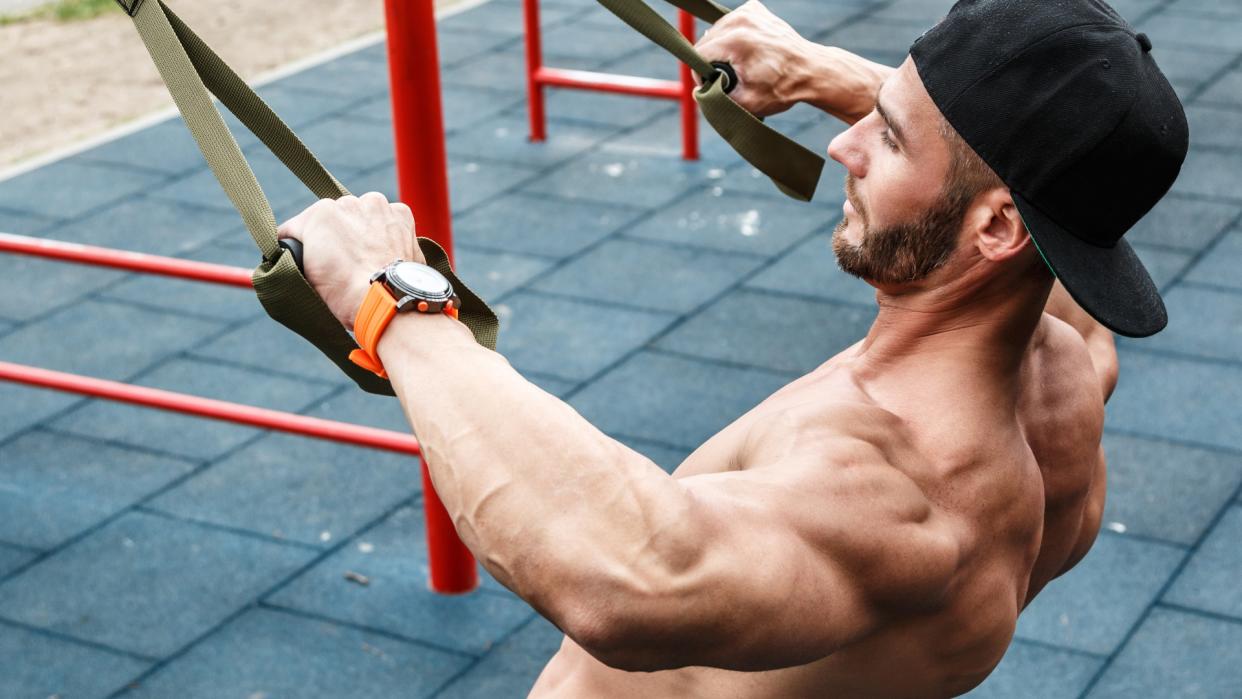  Man outdoors training back workout performing a row using a suspension trainer . 