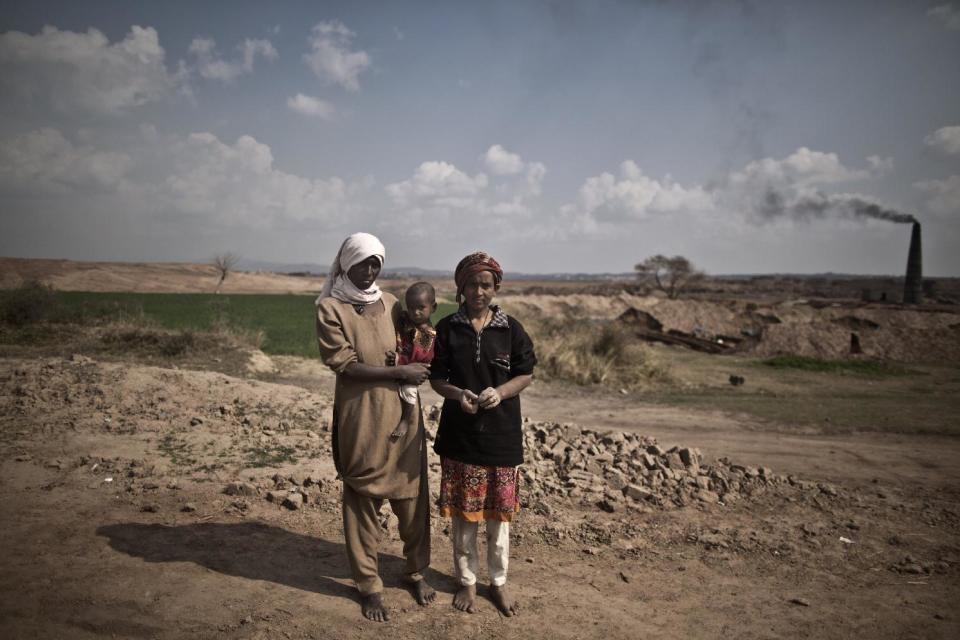 In this Sunday, March 2, 2014, photo, Nusrat Azhar, 29, holding her daughter, Noor, 1 1/2, and her sister Shaziyya, 33, a brick factory workers, pose for a picture at the site of their work on the outskirts of Islamabad, Pakistan. Nusrat and Shaziyya inherited their father's debt to their employer the amount of 400,000 rupees (approximately $4000). (AP Photo/Muhammed Muheisen)
