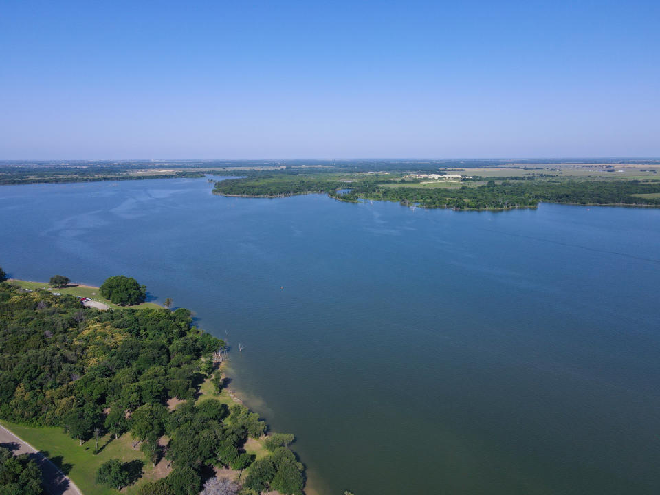 Aerial view of a large serene lake surrounded by lush greenery, with distant horizons under a clear sky