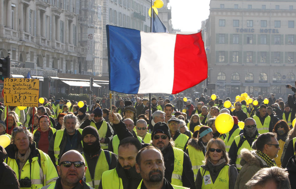 Demonstrators wearing their yellow vests brandish a French flag during a demonstration in Marseille, southern France, Saturday, Dec. 29, 2018. The yellow vest movement held several peaceful demonstrations in cities and towns around France, including about 1,500 people who marched through Marseille. (AP Photo/Claude Paris)