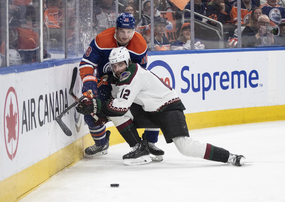 Arizona Coyotes' Connor Mackey (12) and Edmonton Oilers' Zach Hyman (18) battle for the puck during the second period of an NHL hockey game in Edmonton, Alberta, Wednesday, March 22, 2023. (Jason Franson/The Canadian Press via AP)