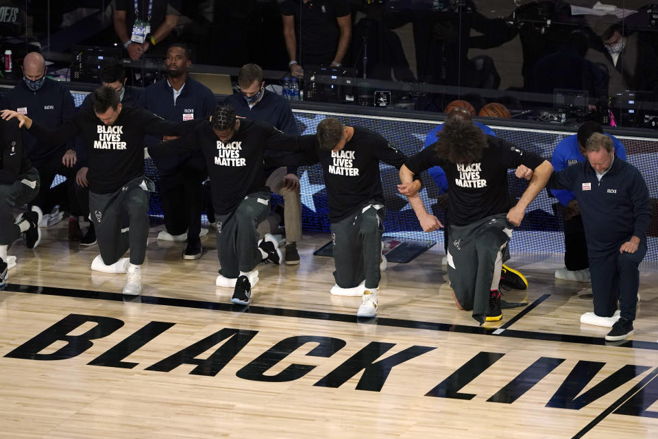 Los Bucks de Milwaukee se arrodillan con los brazos entrelazados durante la interpretación del himno nacional y antes del encuentro de playoffs ante el Magic de Orlando, el sábado 29 de agosto de 2020, en Lake Buena Vista, Florida (AP Foto/Ashley Landis)