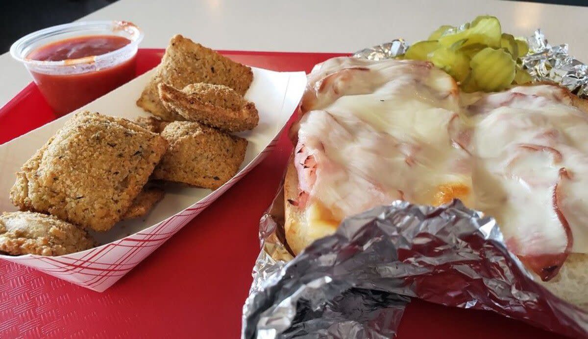 The Gerber Sandwich wrapped in aluminum foil with fried ravioli and mariana sauce on a red tray, Ruma's Deli, St. Louis, on a white table