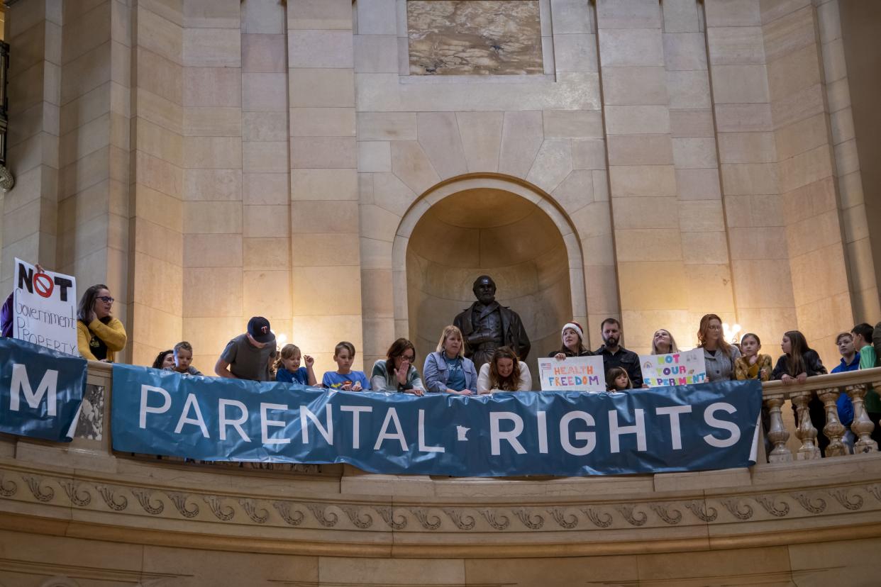 Protesters line a balcony with signs that read: We support health freedom and Parental rights.