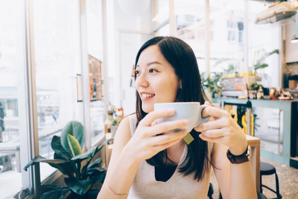 A woman looks out the window of a sunny cafe as she enjoys a cup of coffee