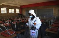 A worker from Bidvest Prestige wearing protective gear, sprays disinfectant in a classroom to help reduce the spread the new coronavirus ahead of the reopening of Landulwazi Comprehensive School, east of Johannesburg, South Africa, Tuesday, May 26, 2020, ahead of the June 1, 2020, re-opening of Grade 7 and 12 learners to school. (AP Photo/Themba Hadebe)