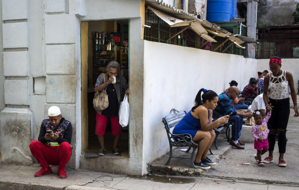 Gente navega en internet en sus teléfonos móviles junto a una plaza en La Habana, Cuba, el 6 de diciembre de 2018. (AP Foto/Desmond Boylan)