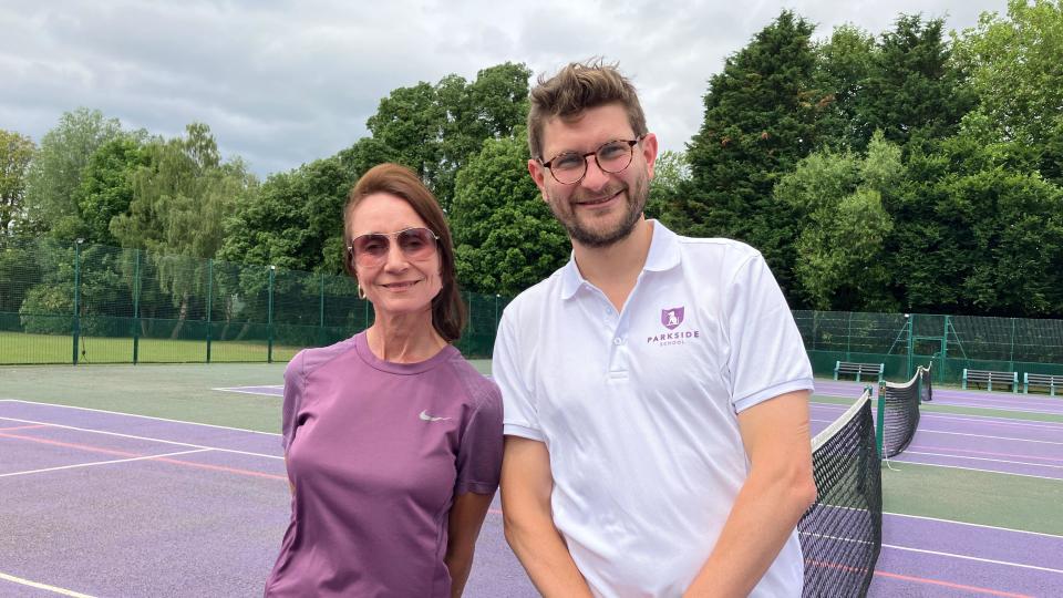 A woman and a man stand at a tennis net smiling