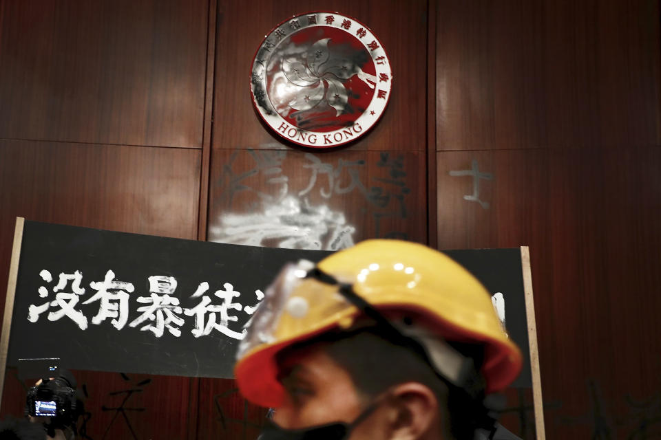 A protester walks by a defaced Hong Kong emblem and a banner reads "No thug, only tyranny" after they broke into the Legislative Council building in Hong Kong, Monday, July 1, 2019. Protesters in Hong Kong took over the legislature's main building Monday night, tearing down portraits of legislative leaders and spray painting pro-democracy slogans on the walls of the main chamber. (AP Photo/Vincent Yu)