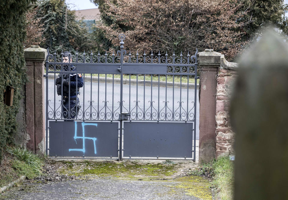 A gendarme guards the Jewish cemetery where the gate and tombs were tagged swastikas are pictured in the Jewish cemetery of Quatzenheim, eastern France, Tuesday, Feb.19, 2019. Marches and gatherings against anti-Semitism are taking place across France following a series of anti-Semitic acts that shocked the country. (AP Photo/Jean-Francois Badias)