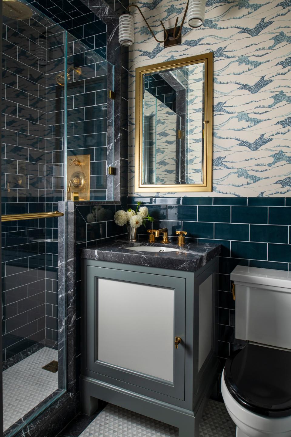 AFTER: The primary bathroom is a brooding escape that harks to the briny deep sea. Dark blue tile by Waterworks and polished brass hardware serve as calming antidotes to one another. The wallpaper is Brook Perdigon’s Toile de Terrain in Lake.