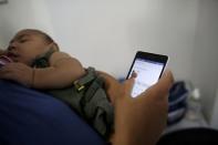 Jaqueline, 25, holds her five-month-old daughter Laura as she uses her mobile phone at the end of an evaluation session with a physiotherapist at the Casa da Esperanca Hospital (Hope House Hospital) in Santos, Sao Paulo state, Brazil April 20, 2016. REUTERS/Nacho Doce