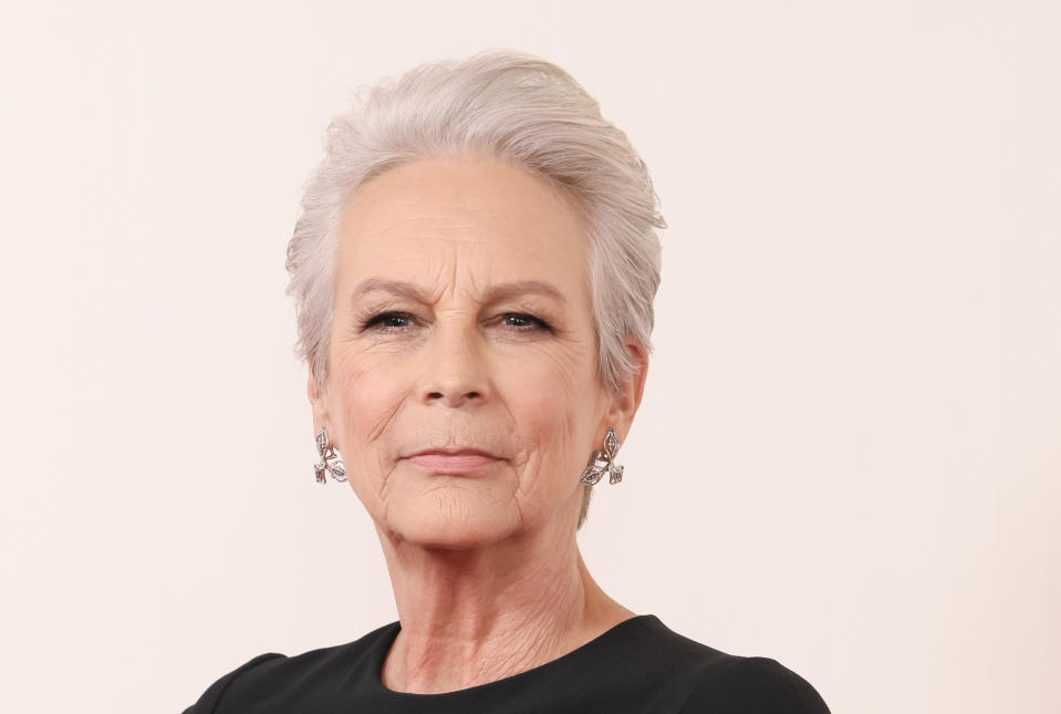 Jamie Lee Curtis poses with a confident expression, wearing a chic, minimalist outfit and statement earrings