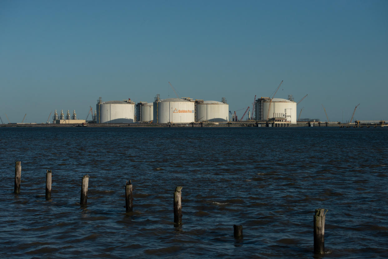 Gas storage tanks seen across the ocean past the posts of a rotting jetty.