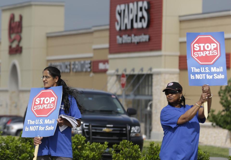 Postal worker Sophia Joseph, left, and retired postal worker Barbara Burkhalter hold signs outside a Staples store during a protest in Dallas, Thursday, April 24, 2014. Thousands of postal workers around the nation are expected to picket outside Staples' stores to protest a pilot program of postal counters in the stores that are staffed with Staples employees. (AP Photo/LM Otero)