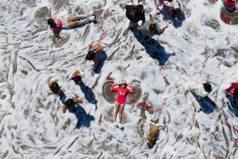 Un niño hace la figura de un ángel mientras otros juegan en una calle cubierta de espuma durante una actividad de verano, en Tongoy, Chile, el 25 de enero de 2024. (AP Foto/Matías Basualdo)