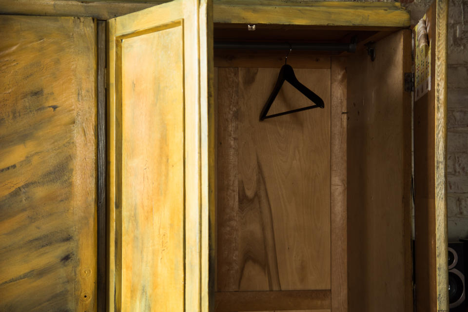 An empty wooden wardrobe is open, revealing an interior with a single black hanger