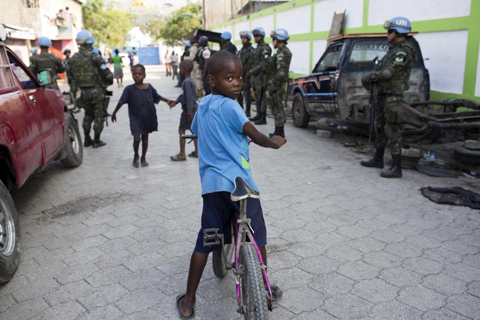 In this Feb. 22, 2017 photo, children play in the street while U.N. peacekeepers from Brazil patrol in the Cite Soleil slum, in Port-au-Prince, Haiti. It took U.N. troops three years to gain control over the sprawling district of Cite Solel, but it's now placid even though its residents still live in desperate poverty. (AP Photo/Dieu Nalio Chery)