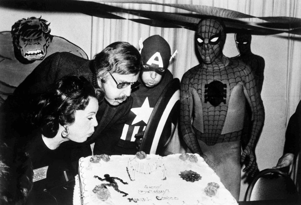 Mighty Marvel comic-book publisher Stan Lee, center left, blows out the candles on the Marvel Comics birthday cake at opening day ceremonies of the First Mighty Marvel Comic Book Convention, March 22, 1975, in New York. At left is Lee&rsquo;s wife, Joan, and on far right is Captain America and Spider-Man.&nbsp;