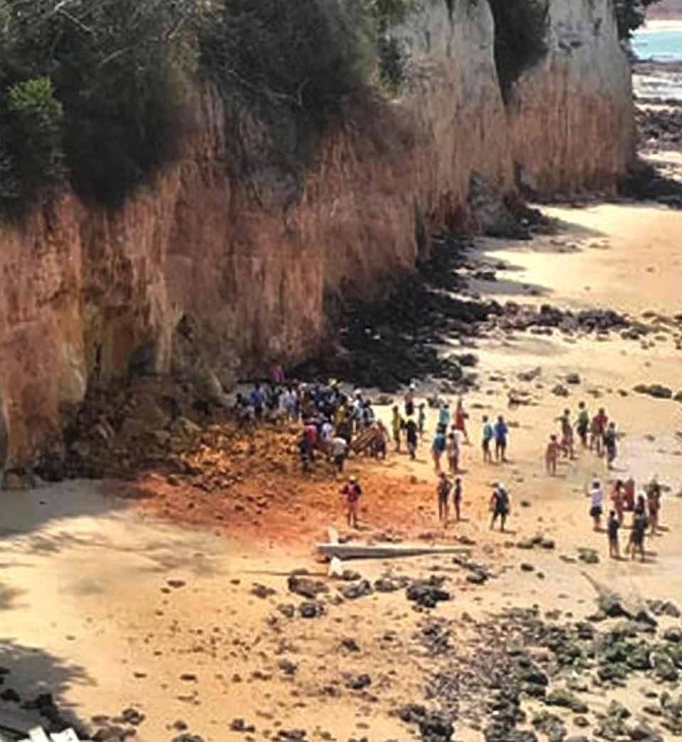 Pictured are a crowd of people surround the scene where the cliff collapse killed the family at Pipa Beach.