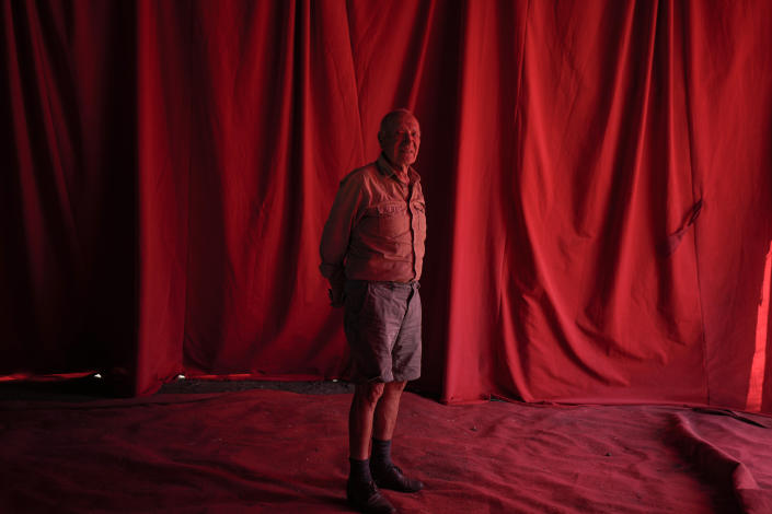 Founder of the Timoteo Circus René Valdés poses for a photo under a red canopy on the show’s current lot, on the outskirts of Santiago, Chile, Saturday, Dec. 10, 2022. Valdés, 86, who remembers the letters received over the years, some with praise and others full of insults, retains his sense of humor and believes his show has built spaces of tolerance and helped combat the rigidity of the once conservative Chilean society. (AP Photo/Esteban Felix)