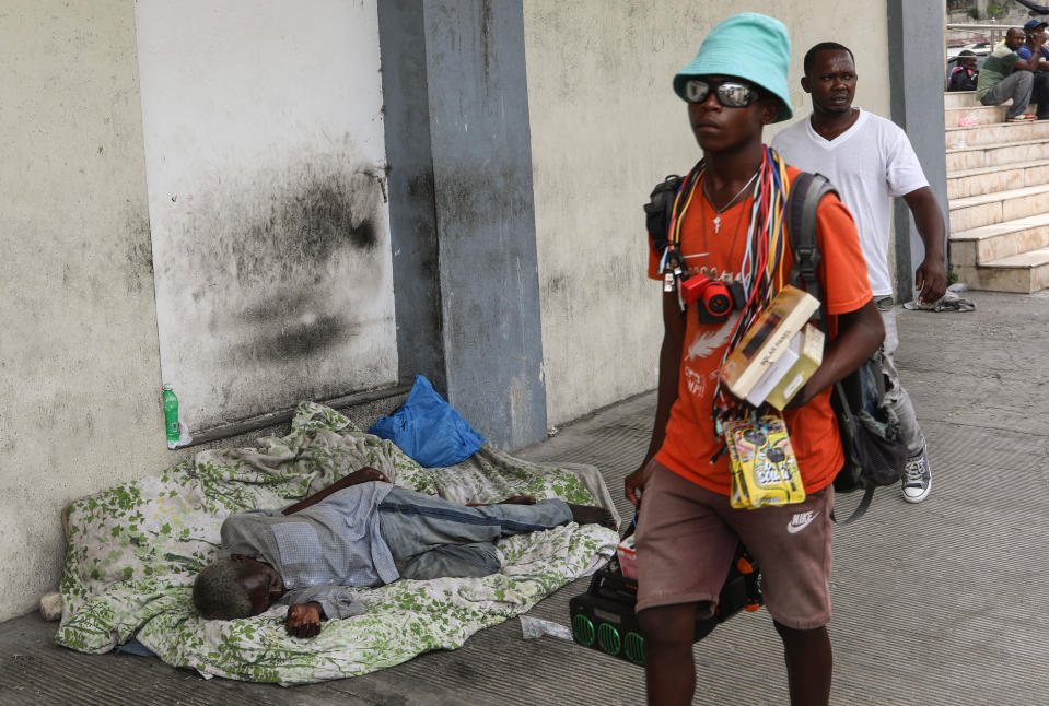 Pedestrians walk past a man sleeping on a street in Port-au-Prince, Haiti, Monday, May 27, 2024. (AP Photo/Odelyn Joseph)