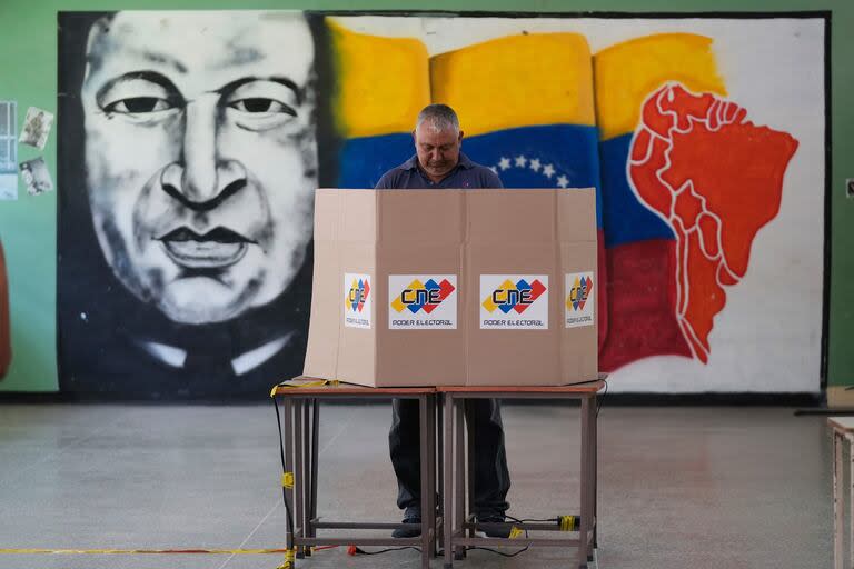 Un votante elige a su candidato frente a un mural del fallecido presidente venezolano Hugo Chávez durante las elecciones presidenciales en Caracas, Venezuela, el domingo 28 de julio de 2024