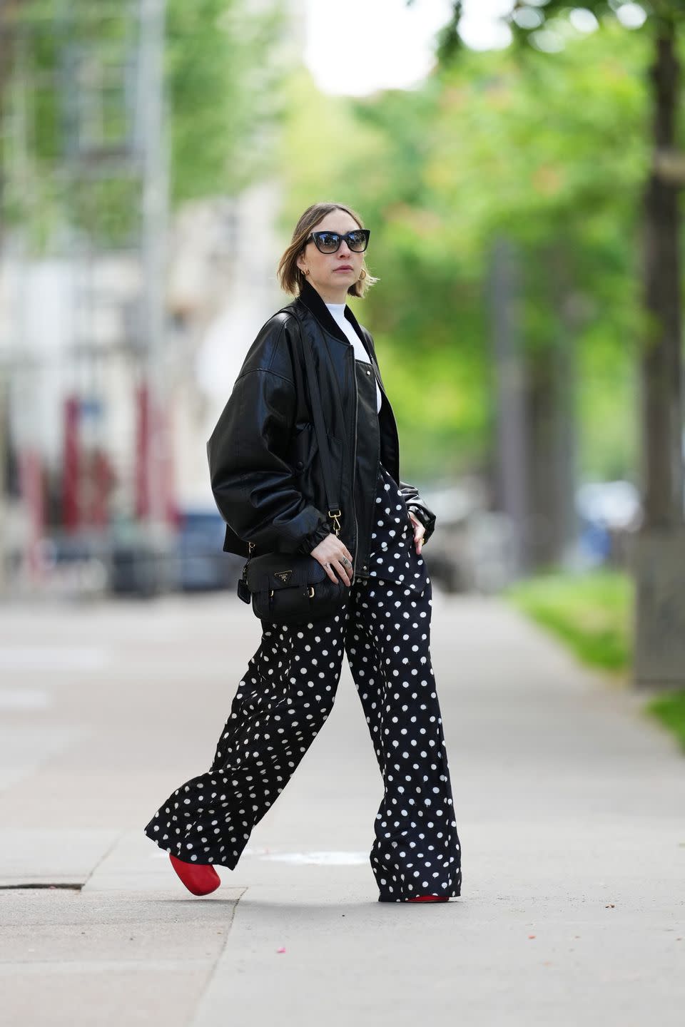 paris, france april 21 emy venturini wears dite eyewear paris sunglasses, a white intimissimi bodysuit, a black leather bomber jacket, black and white balenciaga polka dots pants, a black leather prada bag, golden chloe rings, red leather bottega veneta shoes, during a street style fashion photo session, on april 21, 2024 in paris, france photo by edward berthelotgetty images