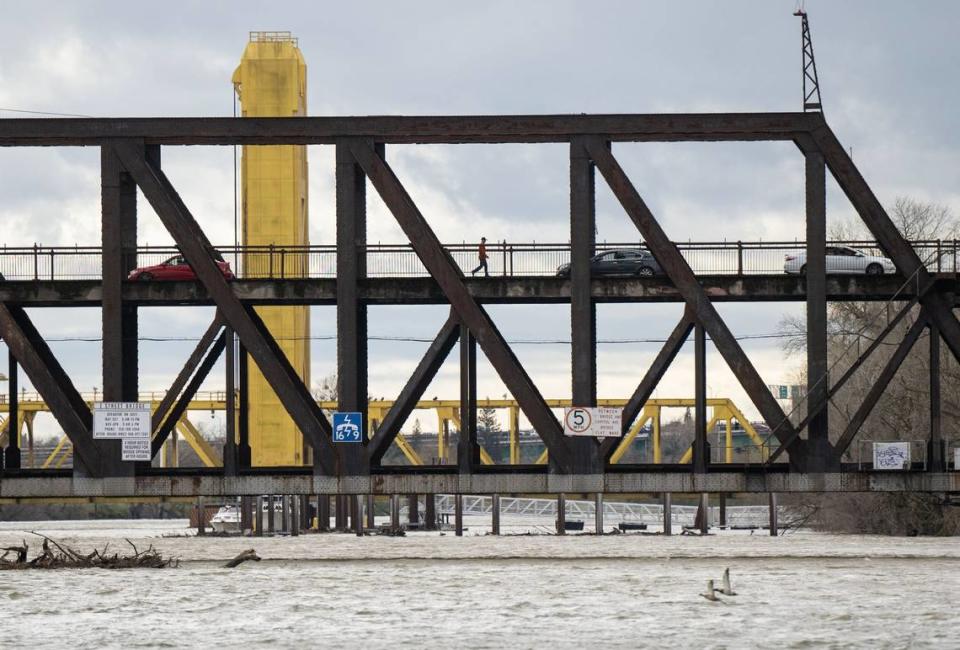 The Sacramento River, at its highest level of the year to date, flows under the I Street Bridge on Tuesday, March 14, 2023, as a pedestrian walks and cars drive on its upper level.