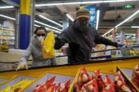 Customer in protective mask grabs potato chips while riding an escalator inside a supermarket, as the country is hit by an outbreak of the novel coronavirus, in Beijing